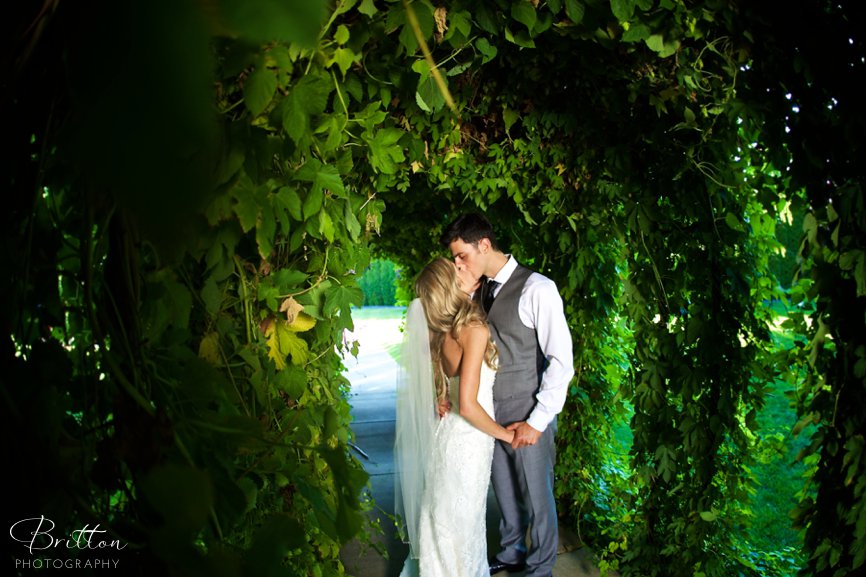 Bride and groom kissing under a hops arbor at Promise Garden